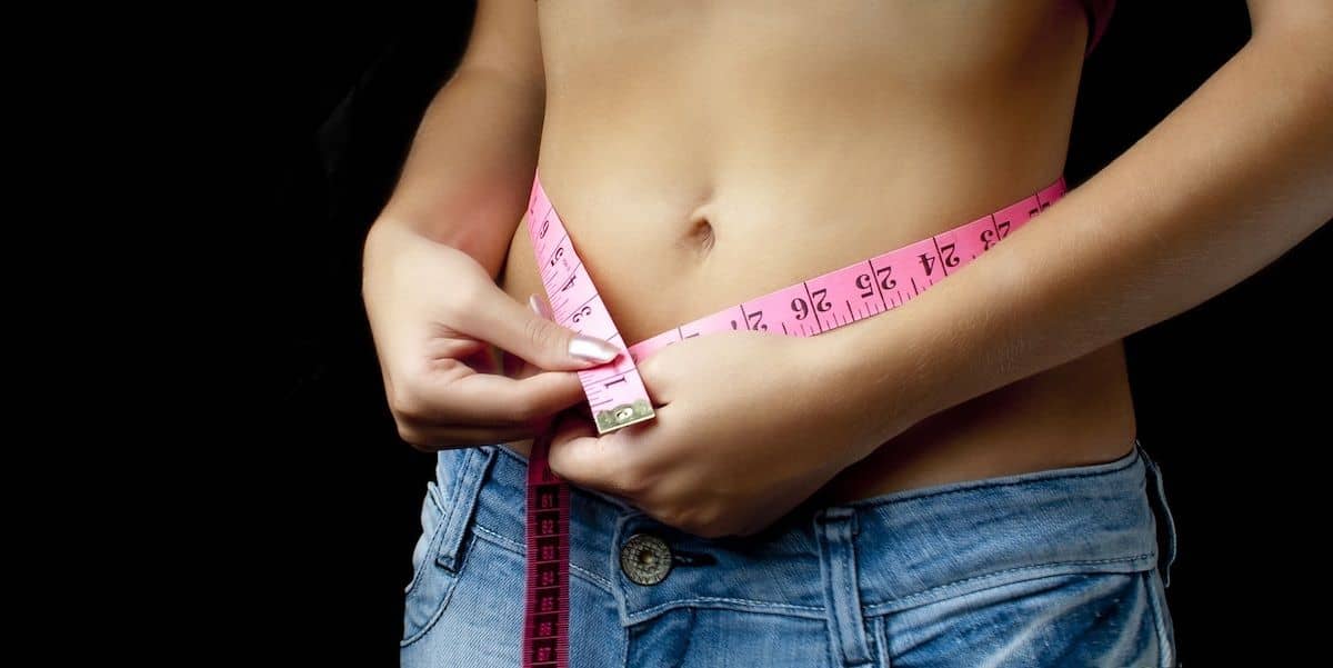Chica joven midiendo su barriga altura ombligo - ejercicios para adelgazar de forma saludable